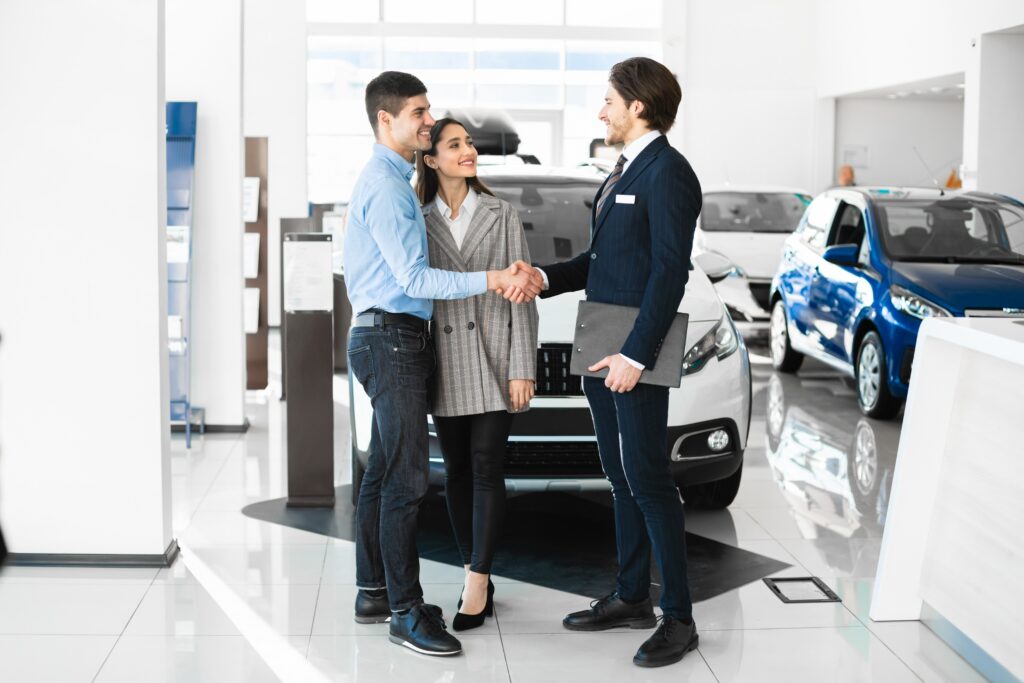 Car Salesman Shaking Hands with a Man. A woman stands next to him.