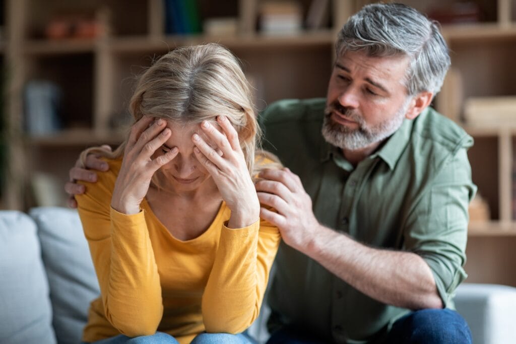 Middle aged man trying to comfort middle aged woman with hands over her face.