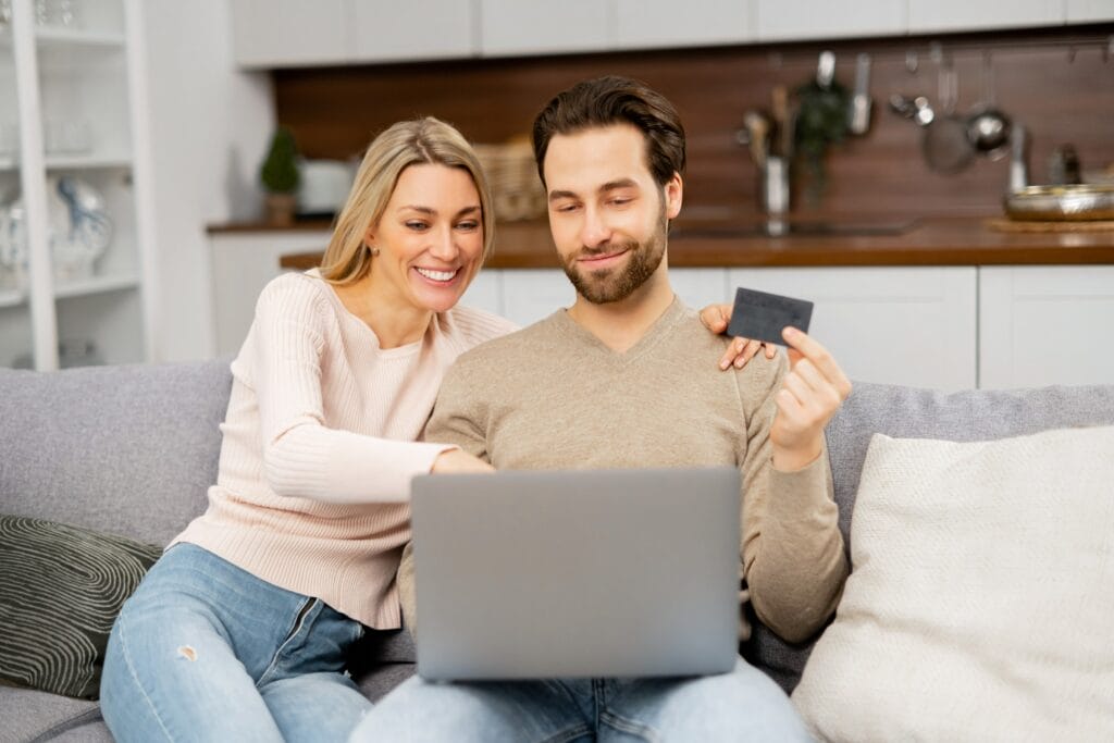 Man and woman sitting on a couch in front of a computer holding a credit card.