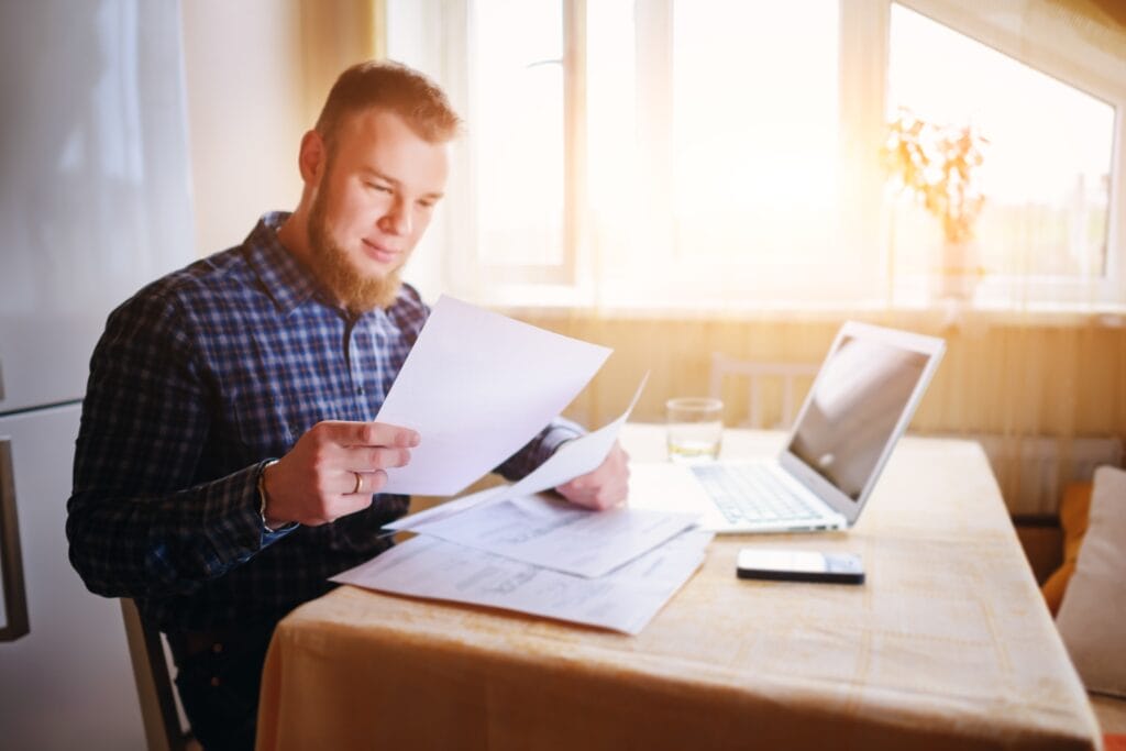 Man sitting at a table with bills around him. A computer is next to him.
