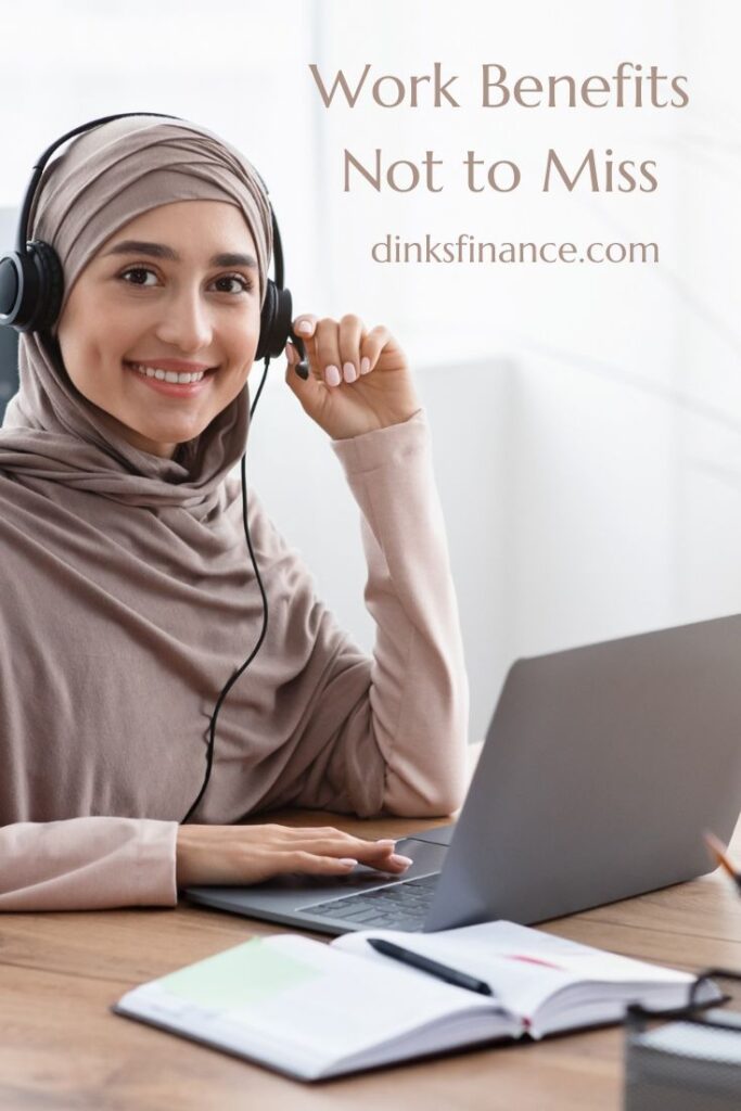 Muslim woman smiling at the camera while working on a laptop with a book open in front of her.