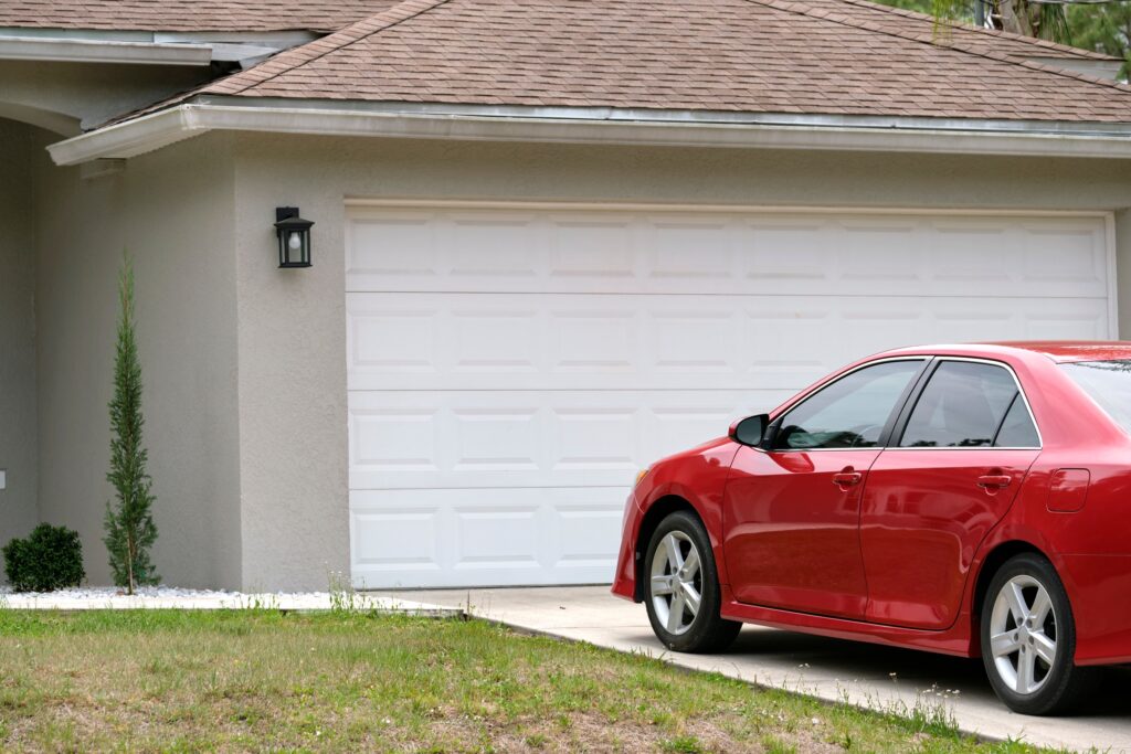 A red car parked in a driveway in front of a closed garage door.
