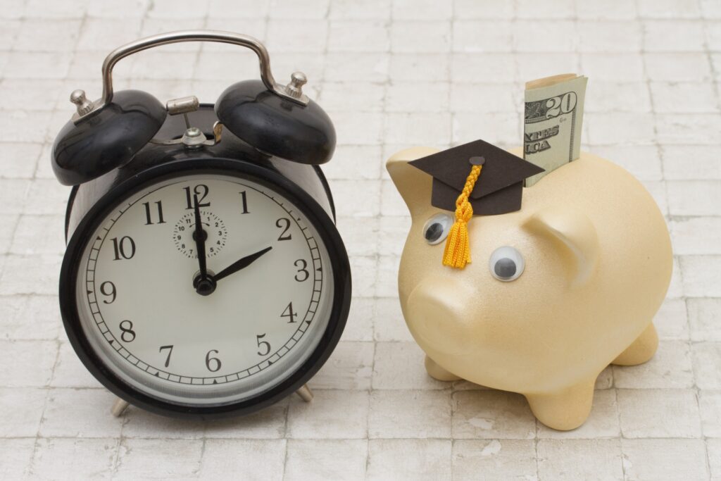 Picture of a clock with a piggy bank beside it. The pig is wearing a graduation