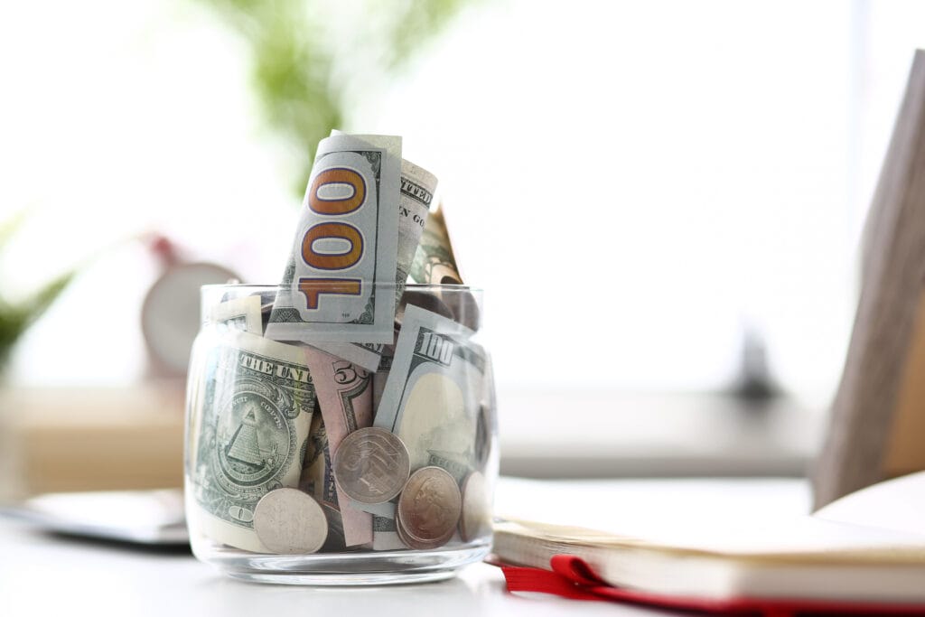 Big jar full of US notes and coins standing on empty worktable